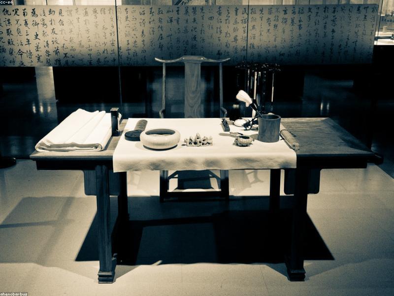 A calligrapher's workspace with ink stone, brush, rice paper, and a freshly written character