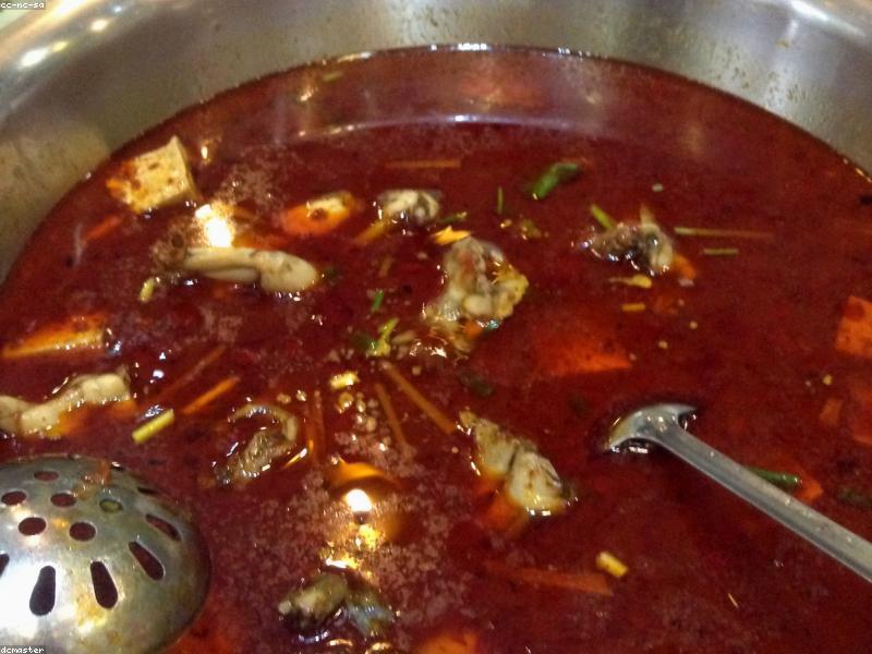 A bubbling split hot pot with red and clear broth surrounded by plates of raw ingredients