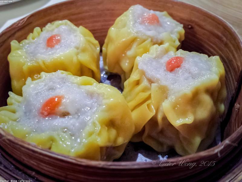 Hands folding dumplings on a wooden cutting board with a bowl of filling